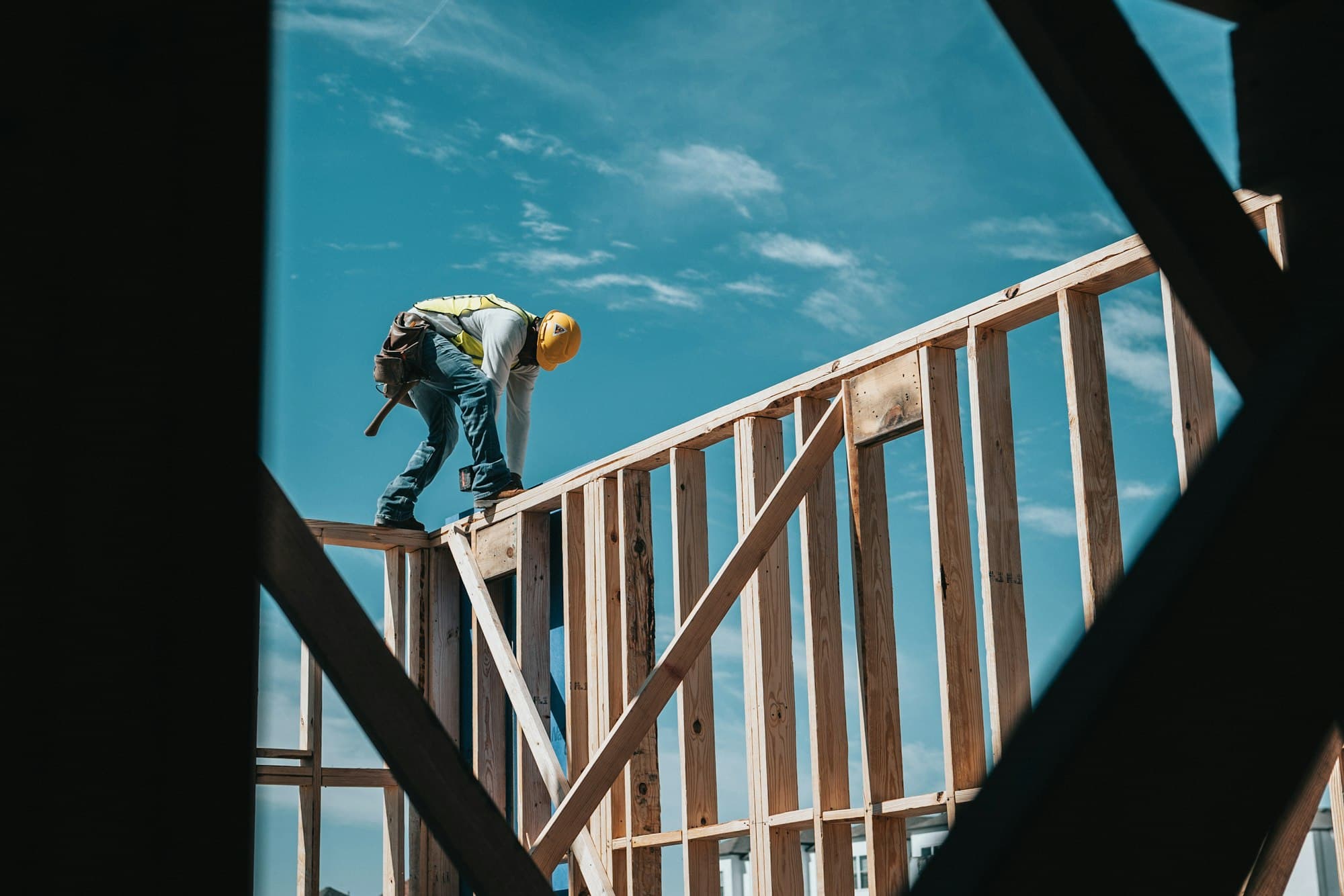 Construction worker in a hard hat and hi-vis vest walking the top plate of a framed wall against the sky